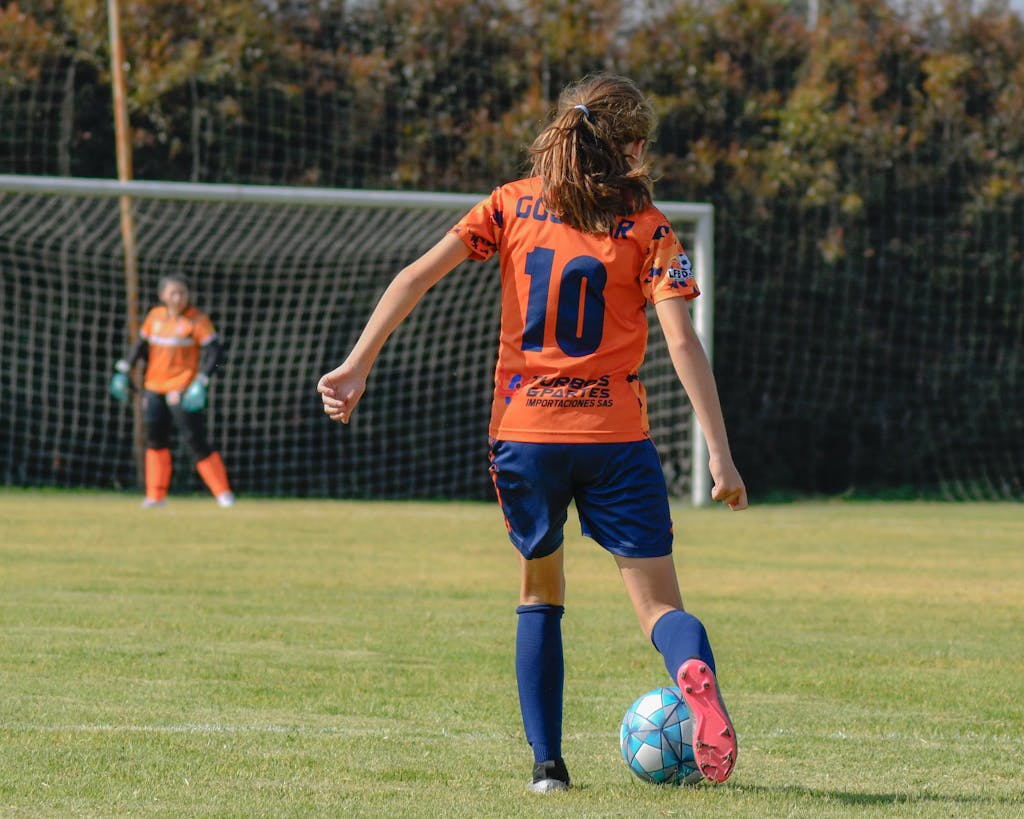 A girl in an orange shirt kicking a soccer ball